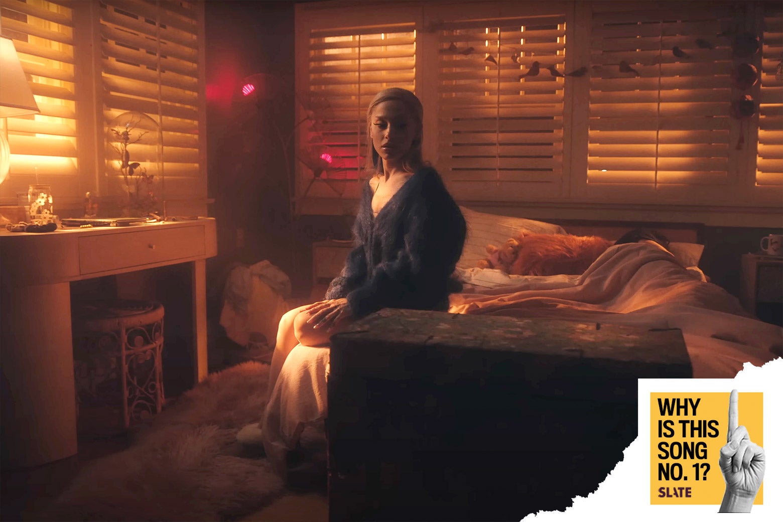A still shows the singer sitting on the side of the bed in the morning light with another figure still asleep behind her. In the corner a logo reads "Why Is This Song No. 1?" and is branded Slate